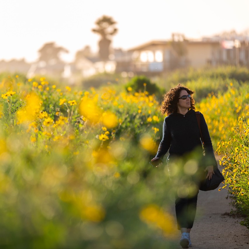 Woman walking through a field of yellow flowers.